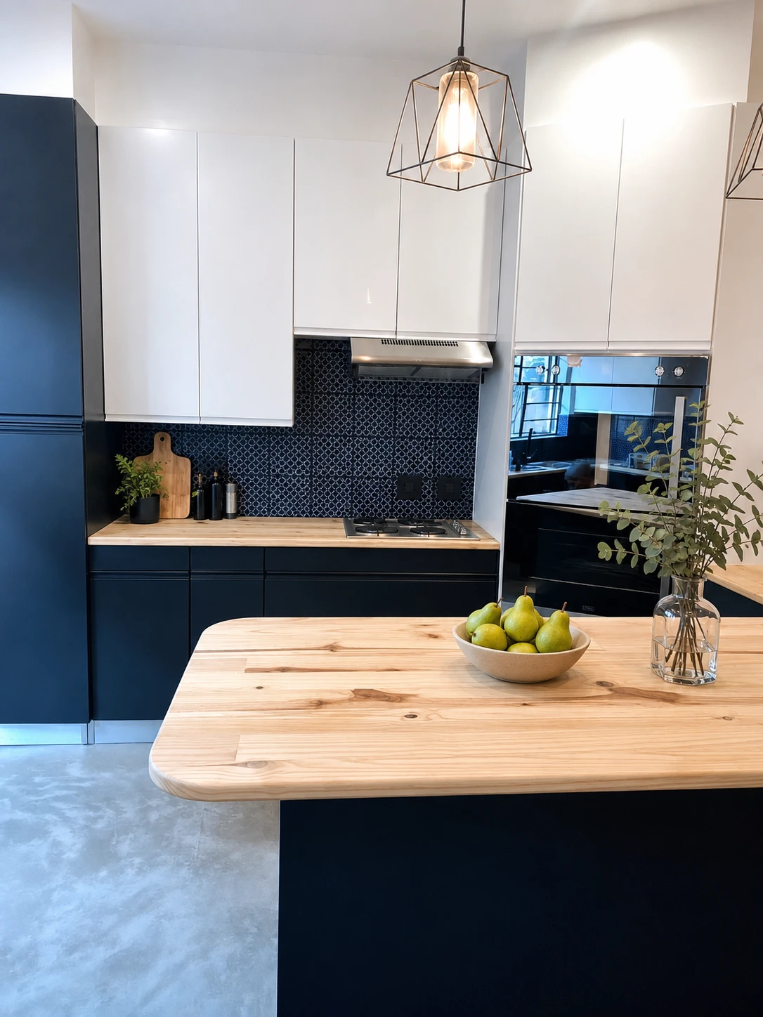 After — Dated white melamine with red trim becomes a bold black and white kitchen. Warm timber counters, a graphic mosaic backsplash and a geometric cage pendant redefine the space without changing the layout.