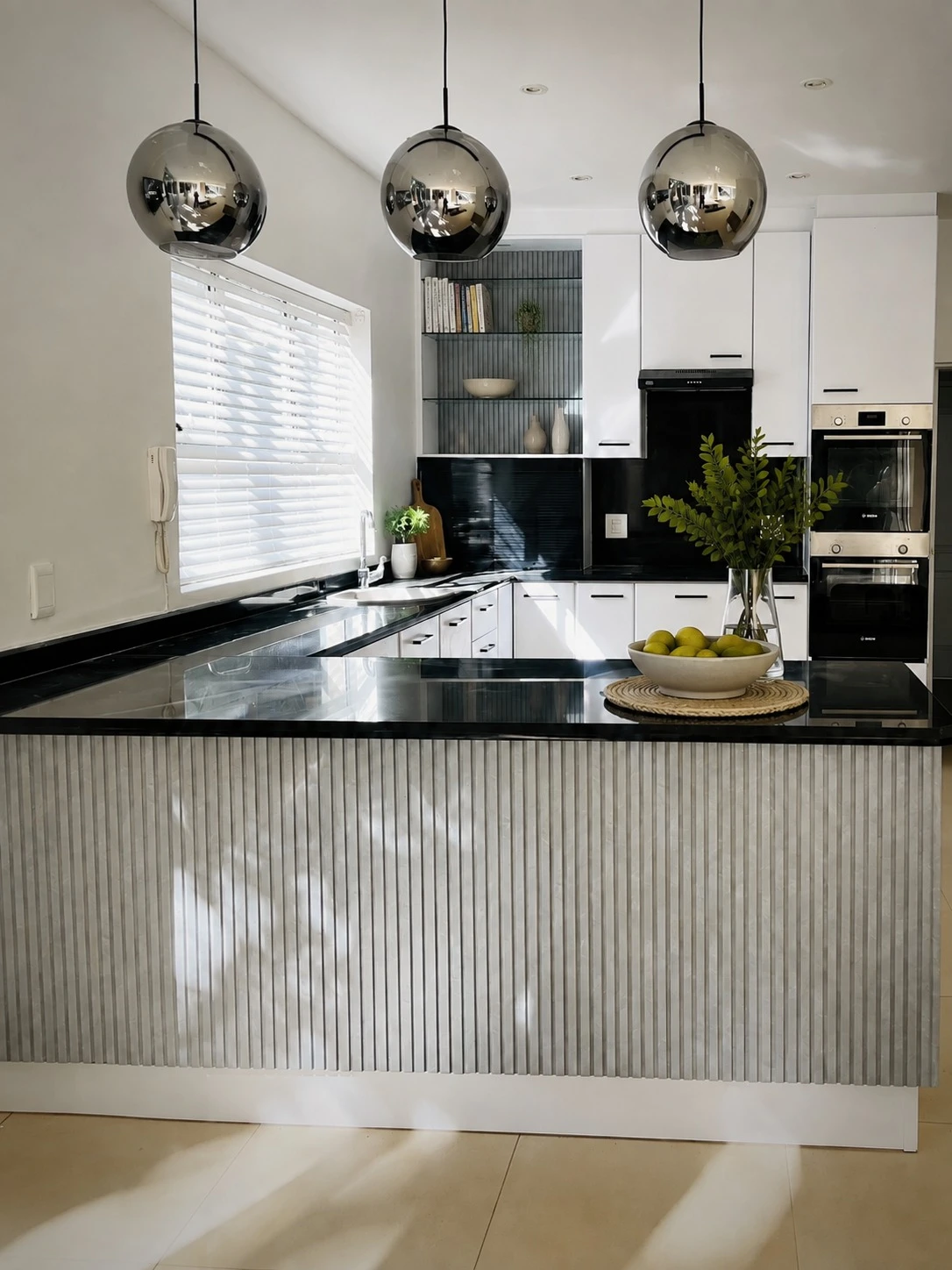 After — Orange-toned timber cabinetry wrapped in satin white, with a fluted sage-grey peninsula for quiet contrast. Slim black handles, smoked-chrome pendants and open shelving give the same kitchen a new personality.