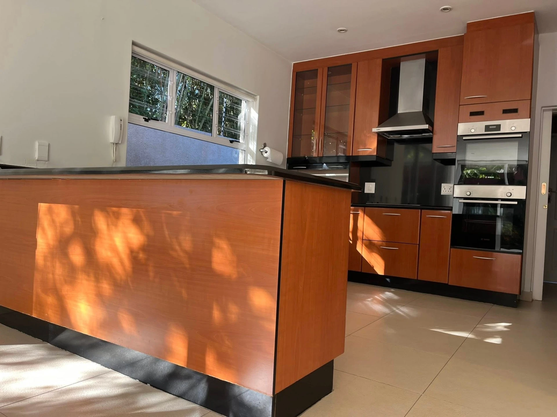 Before — Orange-toned timber cabinetry wrapped in satin white, with a fluted sage-grey peninsula for quiet contrast. Slim black handles, smoked-chrome pendants and open shelving give the same kitchen a new personality.