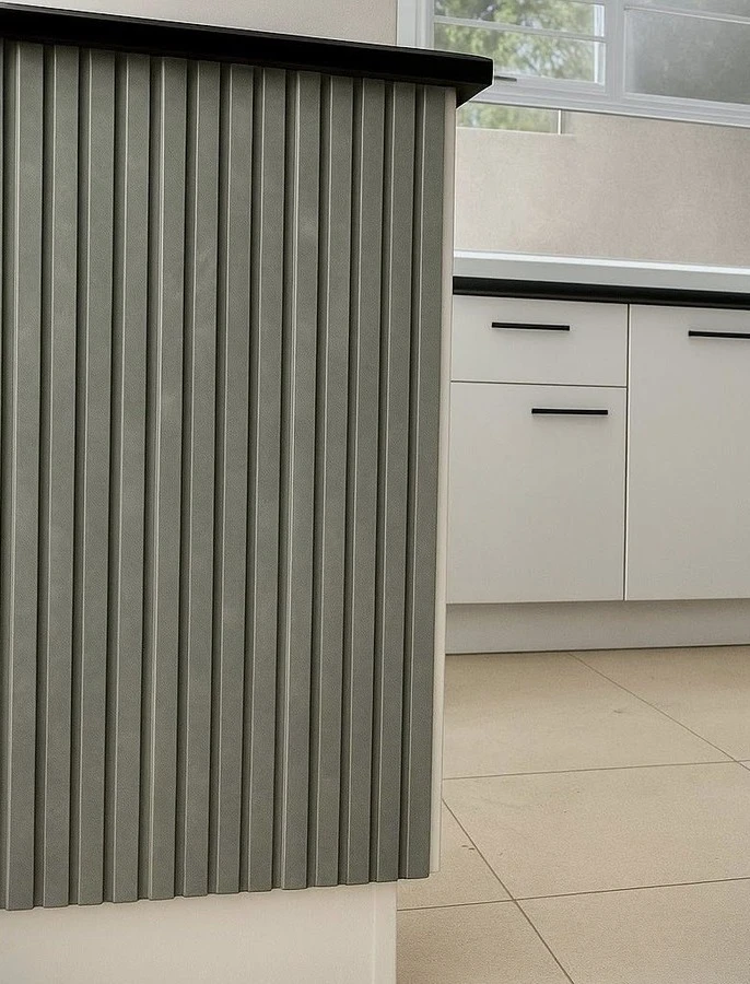 Detail — Orange-toned timber cabinetry wrapped in satin white, with a fluted sage-grey peninsula for quiet contrast. Slim black handles, smoked-chrome pendants and open shelving give the same kitchen a new personality.