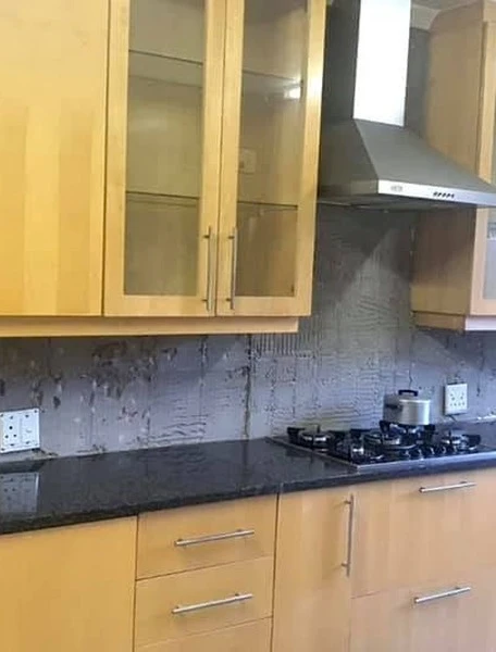 Before — Dated timber cabinetry hand-painted in warm white, slim black handles and a square black-tile backsplash. Existing granite retained — a full change of character with the original kitchen still in place.