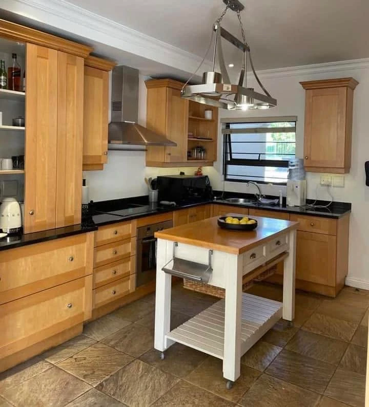 Before — Dated pine shaker cabinetry painted crisp white with matte black hardware. The island was refreshed in place — baskets sprayed, frame painted, top sanded and Monocoat applied — for a complete shift without replacement.
